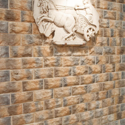Relieve decorativo de piedra blanca con motivo ecuestre montado sobre revestimiento de pared tipo ladrillo cerámico imitación piedra en tonos cálidos, mostrando textura rústica y acabado natural.