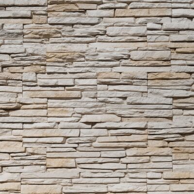Superficie de revestimiento con textura de piedra natural apilada en tonos beige, gris y crema. Las piezas rectangulares presentan acabado mate con relieve que simula estratificación de piedra.
