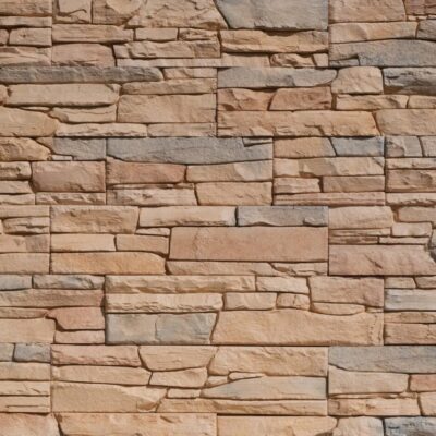 Superficie de revestimiento con textura de piedra natural en tonos beige, gris y arena. Piezas rectangulares de diferentes tamaños dispuestas en patrón irregular con acabado mate y relieve que imita la piedra arenisca.