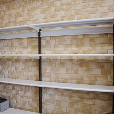 Pared interior revestida con imitación piedra Saboya Aneto en tonos beige y ocre, con acabado texturizado que simula piedra natural. Estanterías metálicas modernas se instalan sobre el revestimiento cerámico.