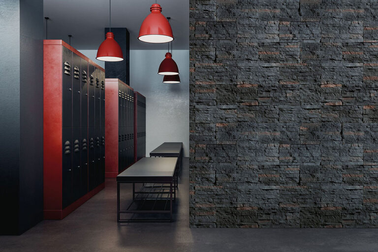 Pasillo con revestimiento de pared tipo piedra gris oscura en formato modular, suelo de cemento pulido, bancos negros minimalistas y tres lámparas colgantes rojas industrial. El revestimiento presenta textura rústica característica del gres porcelanico.