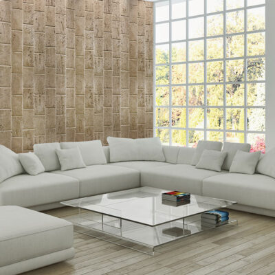 Salón contemporáneo con sofá modular gris claro y revestimiento mural en travertino olivillo oscuro de textura natural. Gran ventanal con vistas al exterior y mesa de centro de cristal blanca.