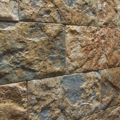 Superficie de revestimiento con textura rugosa imitación piedra en tonos beige y gris, mostrando una trama irregular y acabado mate con variaciones de color natural.