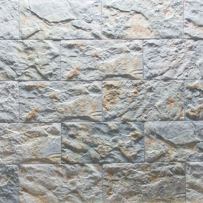 Piezas rectangulares de revestimiento con textura de piedra natural en tonos grises y beige. Acabado mate rugoso con relieve irregular típico de suelo porcelánico efecto cantera.