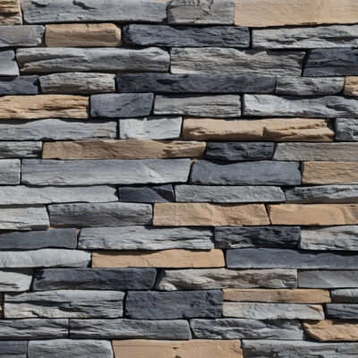 Aplacado de hormigón con efecto piedra natural en tonos grises, negros y beige, piezas irregulares y rectangulares con textura rústica y acabado mate, dispuestas en patrón de hiladas mixtas.