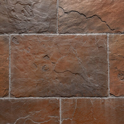 Piezas rectangulares de revestimiento de pared en tonos cobrizo y marrón con textura rústica irregular y acabado mate. Formato de baldosa con juntas grises visibles entre piezas.
