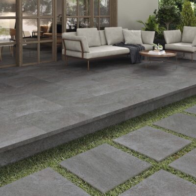 Terraza contemporánea con suelo porcelánico de formato 60x60 en tonos grises grafito, combinado con baldosas de transición y franjas de césped, acompañado de mobiliario de jardín moderno.