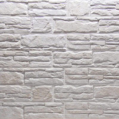 Piezas rectangulares de gres porcelánico con efecto piedra natural en tonos marfil y gris claro, acabado mate con textura rugosa y relieve variable que imita la estratificación de piedra natural.