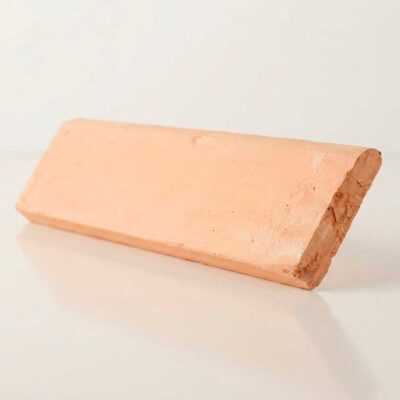 Pieza de zócalo romo de barro con perfil redondeado, formato rectangular alargado, superficie con textura rústica natural en tonos terracota y acabado mate.