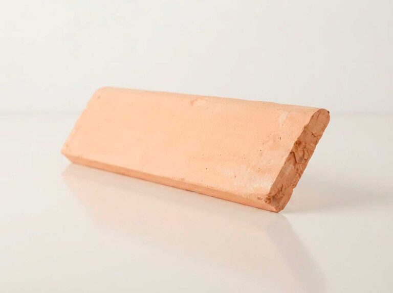 Pieza de zócalo romo de barro con perfil redondeado, formato rectangular alargado, superficie con textura rústica natural en tonos terracota y acabado mate.