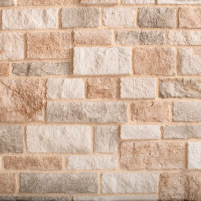 Aplacado de hormigón con imitación de piedra en tonos cálidos beige, tostado y gris. Las piezas rectangulares presentan textura rústica con relieve que simula la corteza natural, acabado mate áspero.
