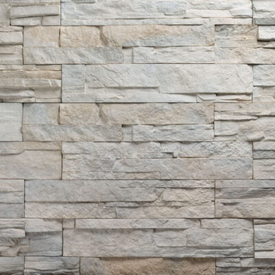 Piezas rectangulares de aplacado imitación piedra natural en tonos beige, gris y tostado con textura irregular y acabado mate, dispuestas en patrón de soga con relieves y profundidad visual.