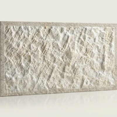 Baldosa cerámica rectangular con textura rústica imitación piedra en tonos beige y gris claro, acabado mate y superficie rugosa con relieve irregular.