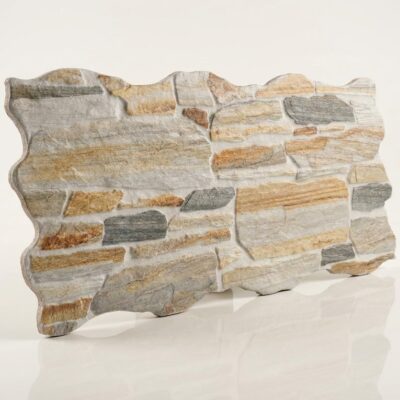 Pieza de azulejo cerámico con formato irregular y acabado mate, que imita la textura de piedra natural. Superficie con tonalidades variadas en gris, beige, ocre y marrón claro, presentando un relieve pronunciado y desigual característica del estilo rústico.