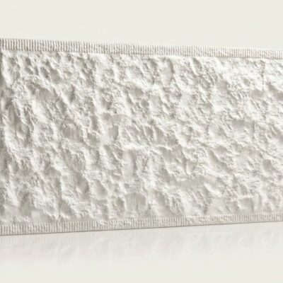 Baldosa cerámica rectangular con textura rugosa que imita piedra natural en tonos marfil y grises claros, acabado mate con borde estriado.