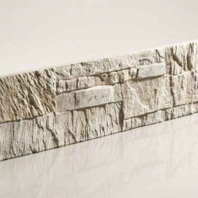 Pieza de azulejo rectangular con textura de piedra natural en tonos marfil y gris claro, acabado rústico con relieve irregular que simula cantería.