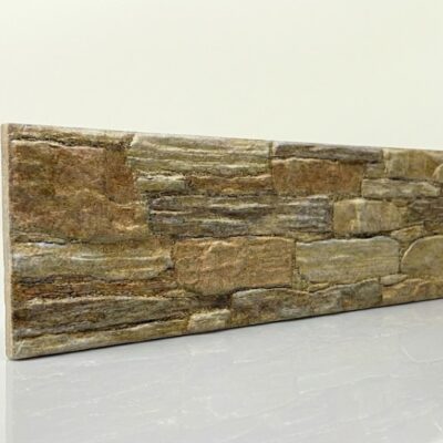 Pieza rectangular de azulejo con acabado efecto piedra natural en tonos beige y gris. Superficie con textura rugosa que imita mampostería de piedra irregular, con variaciones cromáticas y relieves que crean profundidad.