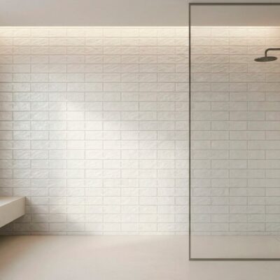 Baño contemporáneo con revestimiento de azulejo imitación piedra en tonos blancos y grises, formato rectangular en patrón de soga. Plato de ducha con mampara de cristal, grifo empotrado y banco flotante blanco.