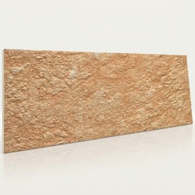 Baldosa cerámica rectangular con textura rústica en tonos ocre y beige, acabado mate que imita piedra natural. Superficie rugosa con variaciones de color y relieve tridimensional.