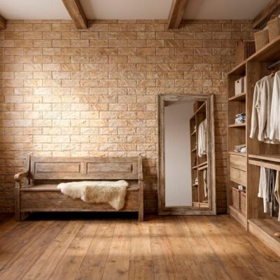 Dormitorio con paredes revestidas de azulejo efecto piedra en tonos beige cálidos, suelo de madera, cama de madera rústica y armario abierto de madera con ropa blanca y accesorios de almacenamiento.