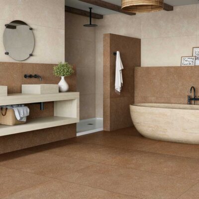 Baño contemporáneo con revestimiento de porcelánico imitación piedra en tonos terracota y beige, suelo porcelánico a juego, bañera freestanding de mármol crema, doble lavabo integrado y espejo circular con marco negro.