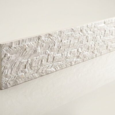 Baldosa rectangular con textura de piedra irregular en tonos crema y beige, acabado mate rugoso que imita la apariencia de piedra natural. Superficie con relieve acusado y variaciones de color.