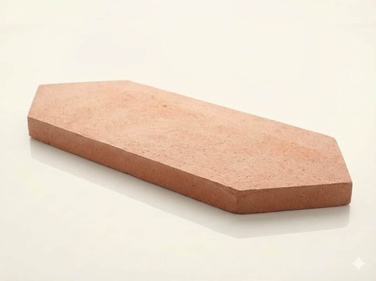 Pieza de barro cocido con forma de rombo alargado, tonos cálidos arena y terracota, superficie mate rústica con textura natural característica del barro cocido.