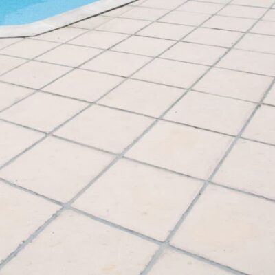 Terraza exterior pavimentada con baldosas de hormigón blanca Nerja en formato rectangular, instaladas en patrón diagonal. Superficie lisa y uniforme junto a borde de piscina azul.
