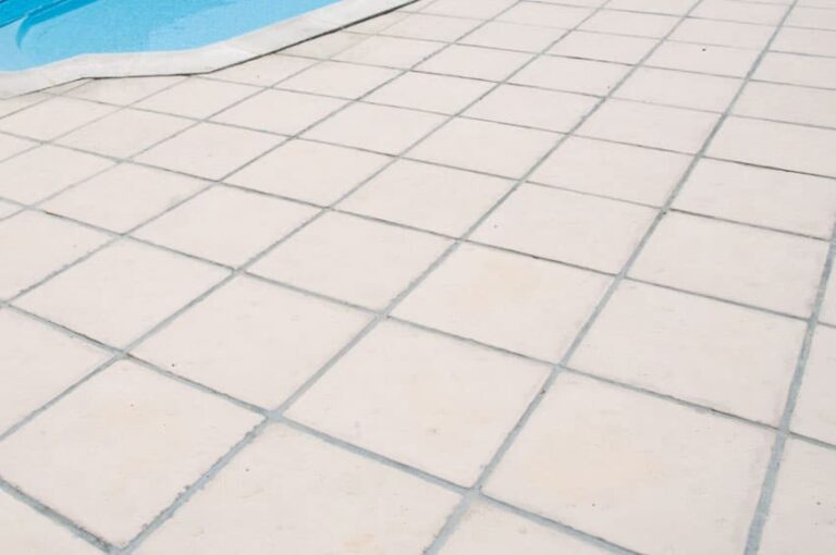 Terraza exterior pavimentada con baldosas de hormigón blanca Nerja en formato rectangular, instaladas en patrón diagonal. Superficie lisa y uniforme junto a borde de piscina azul.