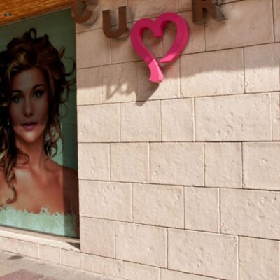 Pared interior revestida con baldosa de hormigón en tonos cálidos ámbar y beige, con textura mate y acabado rústico. A la derecha, decoración con corazón rosa y retrato sobre fondo verde, mostrando la versatilidad del suelo de hormigón para espacios personalizados.