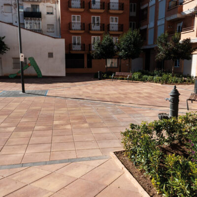 Plaza pública pavimentada con baldosa Goya en tonos terracota y beige, rodeada de edificios residenciales de ladrillo y fachadas de colores claros. Suelo porcelánico con acabado antideslizante y formato rectangular dispuesto en patrón regular.