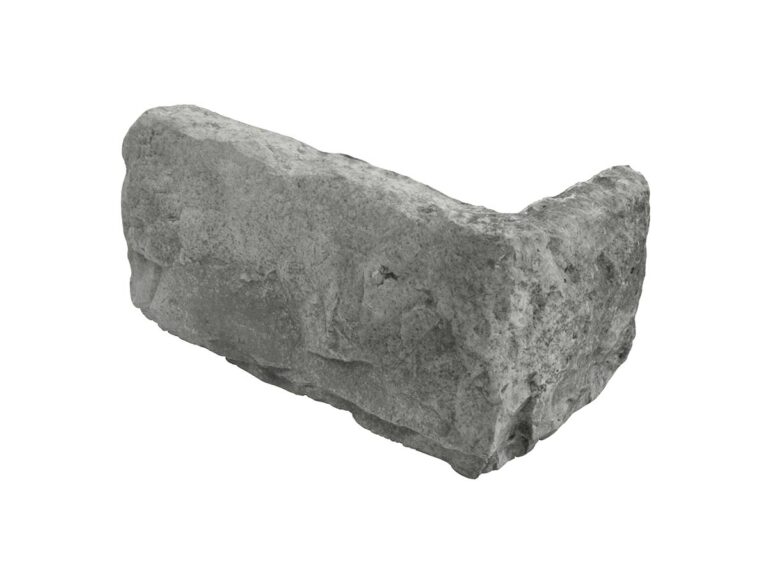 Pieza de esquina irregular en tonos grises con textura rústica que imita piedra natural. Superficie mate con acabado rustico, bordes irregulares y grosor variable típico de aplacados de piedra.