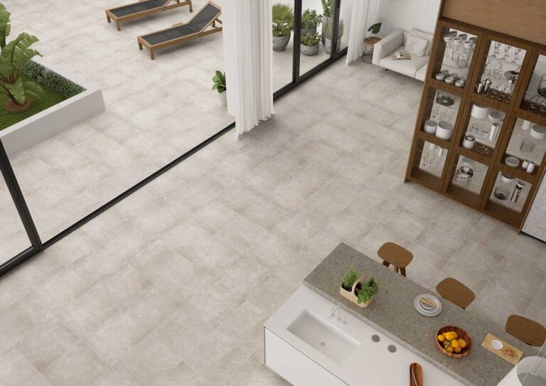 Cocina abierta al exterior con suelo de gres porcelánico en tonos grises naturales, isla central con encimera gris claro, muebles de madera con cristal, y acceso a terraza con tumbonasde madera.