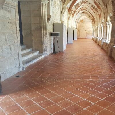 Galería de arcos de piedra con columnas, pavimentada con suelo porcelánico en tonos terracota con acabado mate en formato diagonal. El porcelánico imitación madera proporciona calidez al espacio histórico.