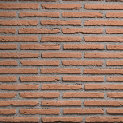 Superficie de ladrillo cerámico visto con textura rústica mate en tonos tierra y naranja rojizo. Piezas rectangulares alargadas dispuestas en hiladas horizontales regulares con juntas de mortero gris claro visibles entre cada ladrillo.