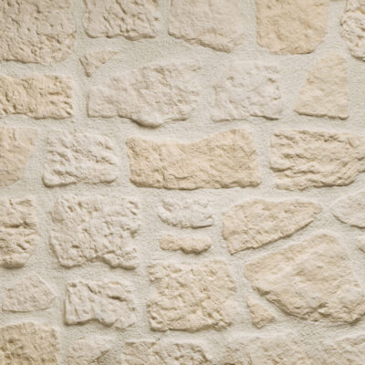 Superficie de revestimiento con textura rústica imitación piedra en tonos beige y dorado, acabado mate con relieve irregular y poros naturales visibles en toda la composición.