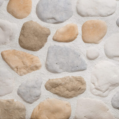 Piezas irregulares de aplacado de hormigón en tonos beige, arena y gris claro con textura rústica de piedra natural, dispuestas sobre fondo blanco neutro.