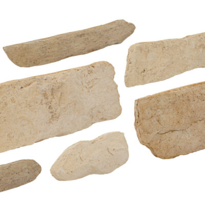 Conjunto de piezas irregulares de revestimiento en tonos beige y arena con textura rústica, acabado mate. Las piezas muestran formas naturales y superficie rugosa característica de piedra natural, ideales para revestimiento de pared.