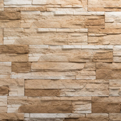 Aplacado de hormigón con acabado rústico en tonos avellana y beige. Piezas rectangulares de diferentes largos en disposición aleatoria, textura rugosa que imita piedra natural apilada, con variaciones de color que generan contraste visual.