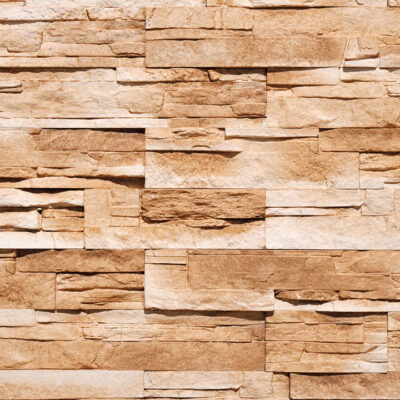 Aplacado de hormigón con efecto piedra en tonos avellana y beige. Piezas rectangulares de diferentes largos en colocación aleatoria, acabado rústico texturizado que imita piedra natural.