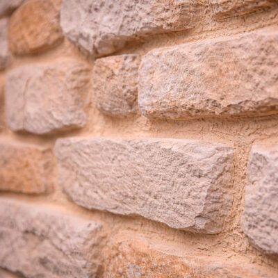 Piezas de aplacado con textura de piedra natural en tonos beige y arena, acabado rústico irregular. Superficie con relieve y variación cromática característica de revestimientos de piedra.
