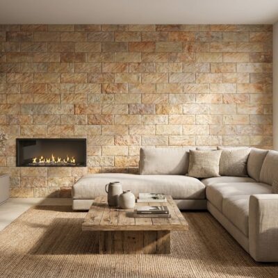 Salón contemporáneo con pared de revestimiento de piedra en tonos ocre y beige, chimenea de bioetanol empotrada, sofá modular gris claro y mesa de centro de madera. El acabado del revestimiento de pared imita piedra natural con textura rugosa y formato rectangular.