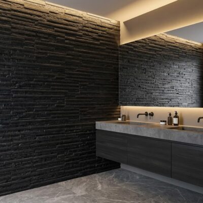 Baño con paredes revestidas en piedra negra texturizada y espejo con iluminación LED integrada. Lavabo de hormigón gris con grifería mural negra, reflejando un diseño minimalista y contemporáneo.