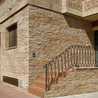 Fachada exterior revestida con piedra natural Plasencia en tonos castaño, mostrando acabado rústico con textura irregular sobre estructura de vivienda residencial.