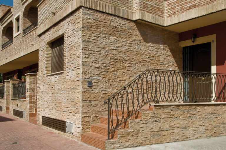 Fachada exterior revestida con piedra natural Plasencia en tonos castaño, mostrando acabado rústico con textura irregular sobre estructura de vivienda residencial.