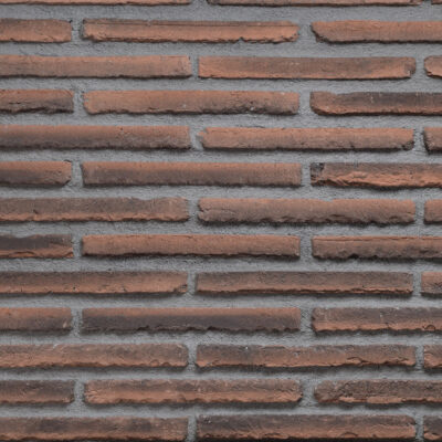 Superficie de aplacado hormigón con efecto ladrillo visto en tonos rojos y marrones oscuros. Textura rugosa y irregular propia del ladrillo cerámico, dispuesta en hiladas horizontales con juntas grises definidas.