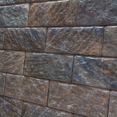 Superficie de revestimiento cerámico con textura de piedra natural en tonos grises y marrones, acabado mate rugoso con vetas diagonales características.