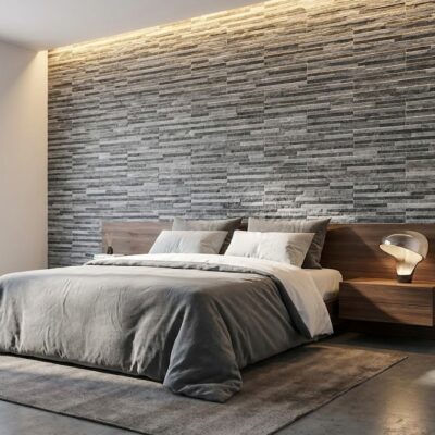 Dormitorio contemporáneo con pared de revestimiento de gres porcelánico efecto piedra en tonos grises y madera. Cama con cabecero de madera oscura, ropa de cama gris y beige, y lámpara de noche integrada en el lateral.