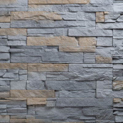 Revestimiento de pared interior en piedra natural gris Varadero con formato de losas irregulares y acabado texturizado. Las piezas en tonos grises y beige están colocadas en patrón aleatorio, creando un efecto de mampostería rústica con relieve pronunciado.
