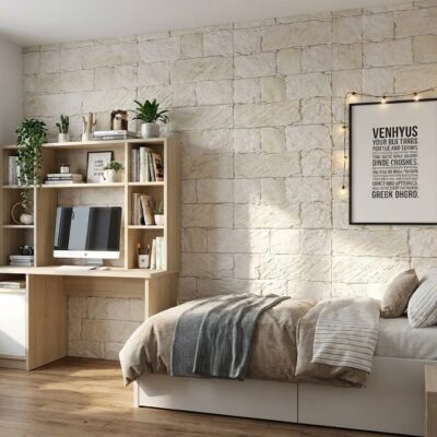 Dormitorio contemporáneo con pared de revestimiento imitación piedra Cárpatos en tonalidad marfil, cama blanca con ropa de cama gris y beige, escritorio de madera clara con estantería integrada y plantas decorativas.